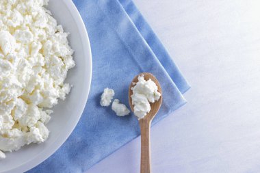Mavi peçete üzerinde süzme peynir. Peynir tahta kaşıkla beyaz tabakta. Yumuşak peynir diyet için. Kahvaltı için sağlıklı süt ürünleri