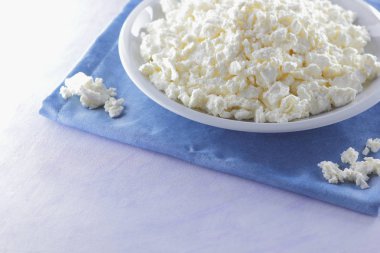 Mavi peçete üzerinde süzme peynir. Peynir tahta kaşıkla beyaz tabakta. Yumuşak peynir diyet için. Kahvaltı için sağlıklı süt ürünleri