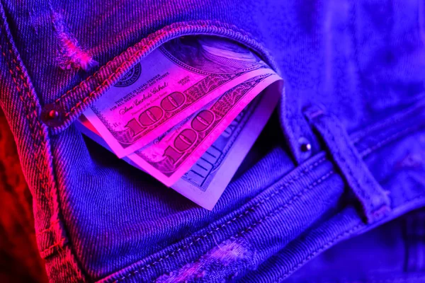 Dollar bills in jeans. Dollars in neon light. Pocket money in creative lighting. Concept