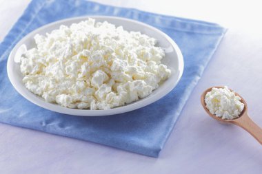 Mavi peçete üzerinde süzme peynir. Peynir tahta kaşıkla beyaz tabakta. Yumuşak peynir diyet için. Kahvaltı için sağlıklı süt ürünleri