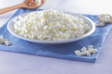 Mavi peçete üzerinde süzme peynir. Peynir tahta kaşıkla beyaz tabakta. Yumuşak peynir diyet için. Kahvaltı için sağlıklı süt ürünleri