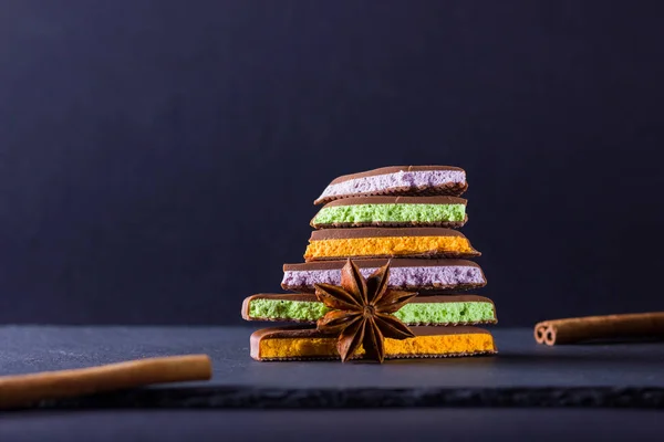 Chocolate with fruit filling on black background. Slices of chocolate with blueberries, mint and orange. Dark chocolate with cinnamon sticks and anise on slate board. Copy space