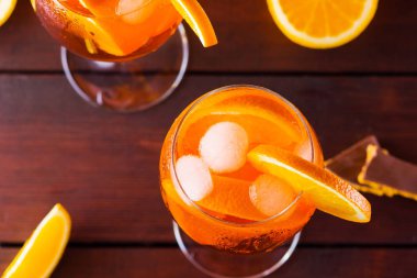 Kokteyl aperol spritz ahşap kurullarında. İki bardak portakal dilimleri ile yaz alkollü kokteyl ile. İtalyan kokteyl aperol spritz ve turuncu ahşap arka plan üzerinde çikolata parçalarını