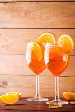 Cocktail aperol spritz on wooden boards. Two glasses with summer alcoholic cocktail with orange slices. Italian cocktail aperol spritz and pieces of chocolate with orange on wooden background clipart