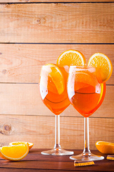 Cocktail aperol spritz on wooden boards. Two glasses with summer alcoholic cocktail with orange slices. Italian cocktail aperol spritz and pieces of chocolate with orange on wooden background