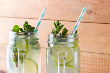 Mojito ve ahşap zemin üzerine nane. Kireç ve ahşap kurullarında taze nane ile kokteyl serinletici. İki kulplu bir yaz içeceği ile narenciye ve buz ile kavanozları. Ev yapımı mojito