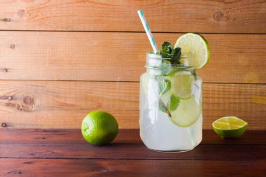 Mojito ve ahşap zemin üzerine nane. Kireç ve ahşap kurullarında taze nane ile kokteyl serinletici. İki kulplu bir yaz içeceği ile narenciye ve buz ile kavanozları. Ev yapımı mojito