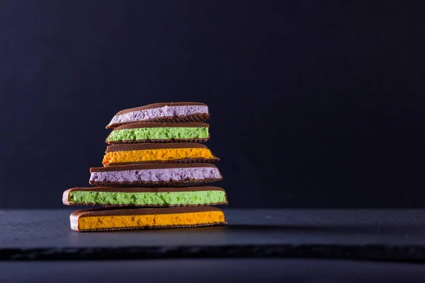 Chocolate with fruit filling on black background. Slices of chocolate with blueberries, mint and orange. Dark chocolate on slate board