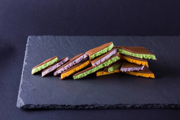 Chocolate with fruit filling on black background. Slices of chocolate with blueberries, mint and orange. Dark chocolate on slate board