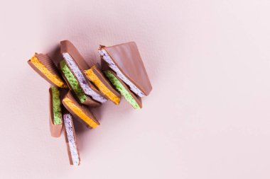 Pembe arka planda meyve dolgulu çikolata. Yaban mersini, nane ve portakal ile çikolata dilimleri. Pastel renkli arka planda koyu çikolata