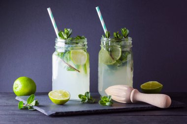 Mojito ve siyah arka plan üzerine nane. Kireç ve kayrak tahta üzerinde taze nane ile kokteyl serinletici. İki kulplu bir yaz içeceği ile narenciye ve buz ile kavanozları. El ile ahşap juicer ve mojito