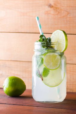 Mojito ve ahşap zemin üzerine nane. Kireç ve ahşap kurullarında taze nane ile kokteyl serinletici. İki kulplu bir yaz içeceği ile narenciye ve buz ile kavanozları. Ev yapımı mojito