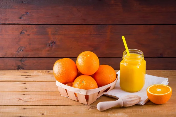 Orange fruits and juice on white napkin. Citrus fruit for making juice with manual juicer. Oranges in wooden box on wooden boards. Mason jar with orange juice
