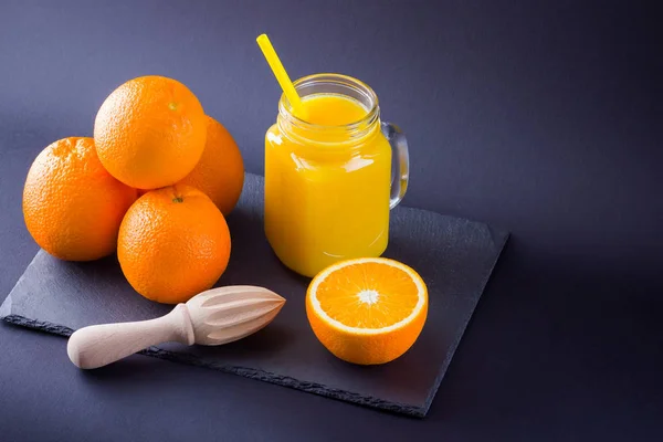 Orange fruits and juice on black background. Citrus fruit for making juice with manual juicer. Oranges on slate board. Mason jar with orange juice. Copy space