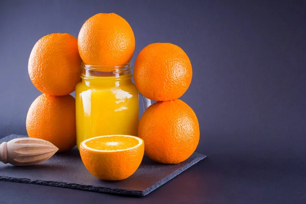 Orange fruits and juice on black background. Citrus fruit for making juice with manual juicer. Oranges on slate board. Mason jar with orange juice. Copy space