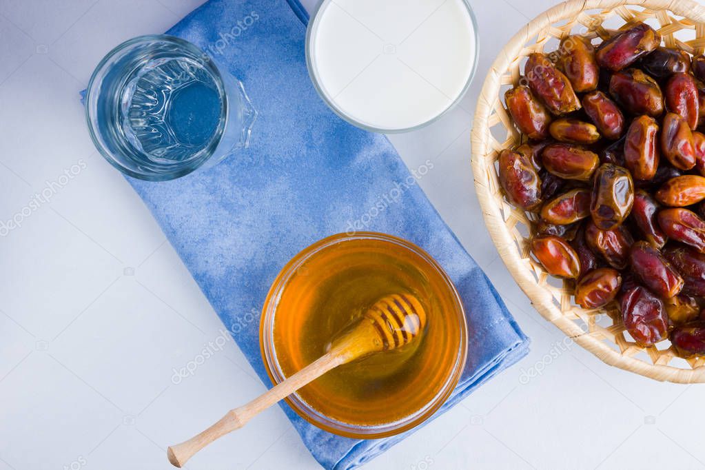 Dried dates, milk and honey on white background. Holy month of Ramadan, concept. Righteous Muslim lifestyle. Starvation. Dates in wooden basket and honey. Vegetarian food. Copy space
