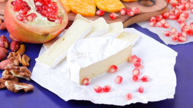 Farklı peynir ve meyve türleri. Dilimlenmiş camembert ve nar. Yumuşak ve sert peynir ve fındık. Camembert ve mavi arka plan üzerinde üzüm. Vejetaryen yemekler