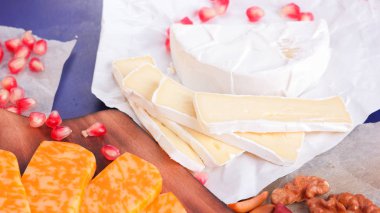 Farklı peynir ve meyve türleri. Dilimlenmiş camembert ve nar. Yumuşak ve sert peynir ve fındık. Camembert ve mavi arka plan üzerinde üzüm. Vejetaryen yemekler
