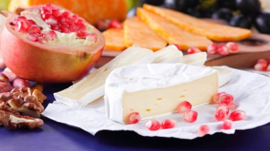 Farklı peynir ve meyve türleri. Dilimlenmiş camembert ve nar. Yumuşak ve sert peynir ve fındık. Camembert ve mavi arka plan üzerinde üzüm. Vejetaryen yemekler