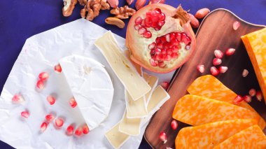 Farklı peynir ve meyve türleri. Dilimlenmiş camembert ve nar. Yumuşak ve sert peynir ve fındık. Camembert ve mavi arka plan üzerinde üzüm. Vejetaryen yemekler
