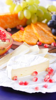 Farklı peynir ve meyve türleri. Dilimlenmiş camembert ve nar. Yumuşak ve sert peynir ve fındık. Camembert ve mavi arka plan üzerinde üzüm. Vejetaryen yemekler