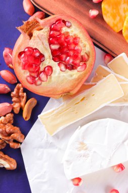 Farklı peynir ve meyve türleri. Dilimlenmiş camembert ve nar. Yumuşak ve sert peynir ve fındık. Camembert ve mavi arka plan üzerinde üzüm. Vejetaryen yemekler