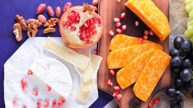 Farklı peynir ve meyve türleri. Dilimlenmiş camembert ve nar. Yumuşak ve sert peynir ve fındık. Camembert ve mavi arka plan üzerinde üzüm. Vejetaryen yemekler