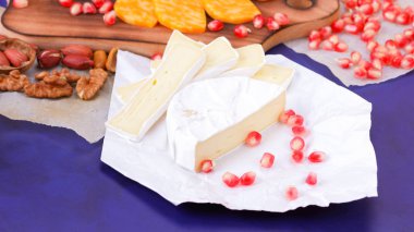 Farklı peynir ve meyve türleri. Dilimlenmiş camembert ve nar. Yumuşak ve sert peynir ve fındık. Camembert ve mavi arka plan üzerinde üzüm. Vejetaryen yemekler