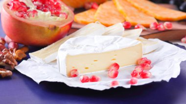 Farklı peynir ve meyve türleri. Dilimlenmiş camembert ve nar. Yumuşak ve sert peynir ve fındık. Camembert ve mavi arka plan üzerinde üzüm. Vejetaryen yemekler