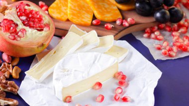 Farklı peynir ve meyve türleri. Dilimlenmiş camembert ve nar. Yumuşak ve sert peynir ve fındık. Camembert ve mavi arka plan üzerinde üzüm. Vejetaryen yemekler