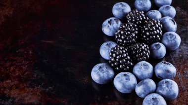 Koyu arka planda yaban mersini ve böğürtlen. Vegan için taze meyveler. Paslı arka planda çeşitli meyveler. Düz yatıyordu