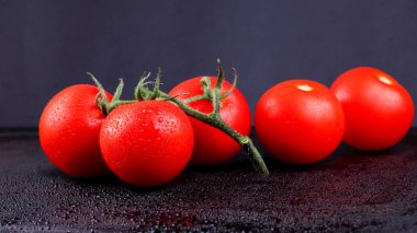 Siyah arka planda kırmızı domatesler. Salata için bir demet domates. Koyu zeminde bahçeden kırmızı sebzeler. Vejetaryen yemekleri. Yan görünüm