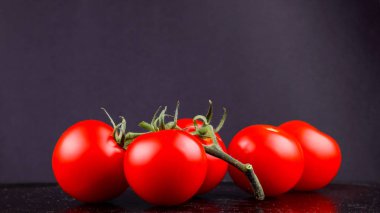 Siyah arka planda kırmızı domatesler. Salata için bir demet domates. Koyu zeminde bahçeden kırmızı sebzeler. Vejetaryen yemekleri. Yan görünüm