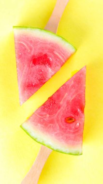 Sarı arka planda sopa üzerine karpuz dilimleri. Renkli arka planda karpuz dondurması. Yaz konsepti. Düz yatıyordu