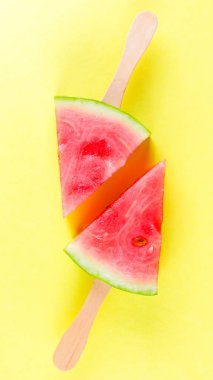 Sarı arka planda sopa üzerine karpuz dilimleri. Renkli arka planda karpuz dondurması. Yaz konsepti. Düz yatıyordu