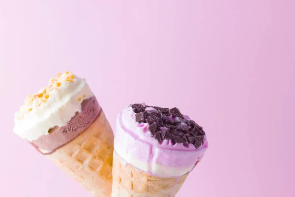 Ice cream with chocolate and nuts on a pink white background. Two ice cream cones in a glass. Summer milk dessert in a waffle cone. Copy space