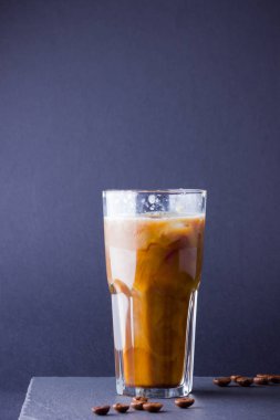 Koyu bir arka plan üzerinde süt ile buzlu kahve. Tahtada kafeinli yaz içkisi. Latte cam bir fincan ve kahve çekirdekleri içinde. Kopyalama alanı