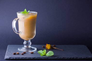 Koyu bir arka plan üzerinde süt ile buzlu kahve. Latte ve taze naneli bir tahtada. Bir bardakta yaz içkisi ve kahve çekirdekleri. Kopyalama alanı