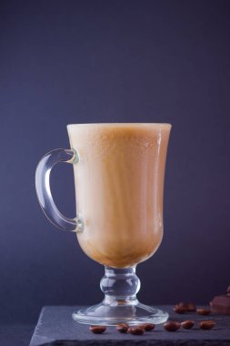 Karanlık bir arka planda süt ile buzlu kahve. Arduvaz tahtasında latte ve siyah çikolata. Bardakta süt içeceği ve kahve çekirdekleri. Boşluk Kopyala