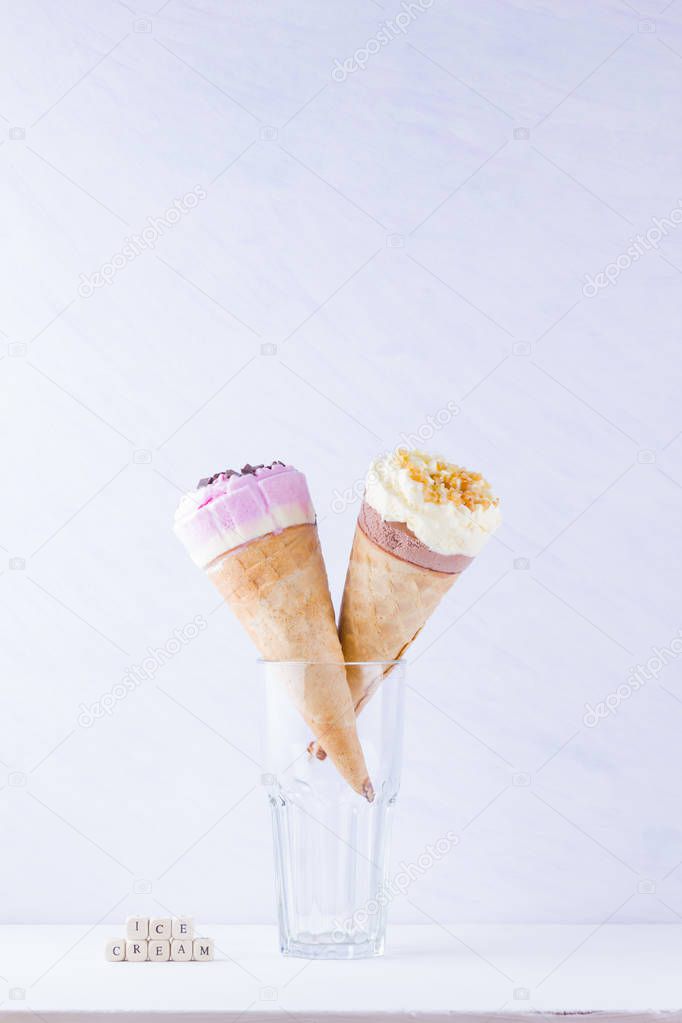 Ice cream with chocolate and nuts on a white background. Two ice cream cones in a glass. Summer milk dessert in a waffle cone. Copy space