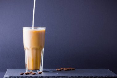 Koyu bir arka plan üzerinde süt ile buzlu kahve. Tahtada kafeinli yaz içkisi. Latte cam bir fincan ve kahve çekirdekleri içinde. Kopyalama alanı