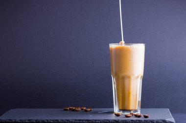Koyu bir arka plan üzerinde süt ile buzlu kahve. Tahtada kafeinli yaz içkisi. Latte cam bir fincan ve kahve çekirdekleri içinde. Kopyalama alanı