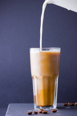 Koyu bir arka plan üzerinde süt ile buzlu kahve. Tahtada kafeinli yaz içkisi. Latte cam bir fincan ve kahve çekirdekleri içinde. Kopyalama alanı