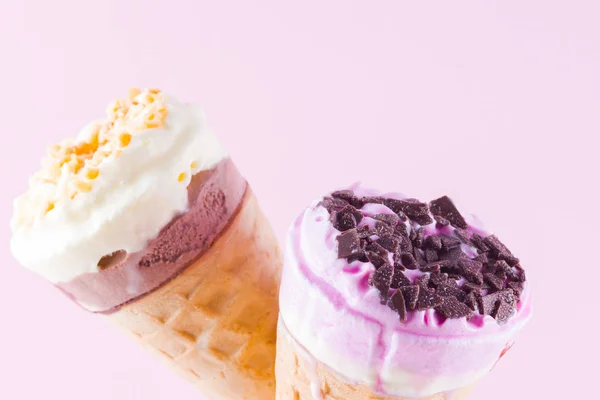 Ice cream with chocolate and nuts on a pink white background. Two ice cream cones in a glass. Summer milk dessert in a waffle cone. Copy space