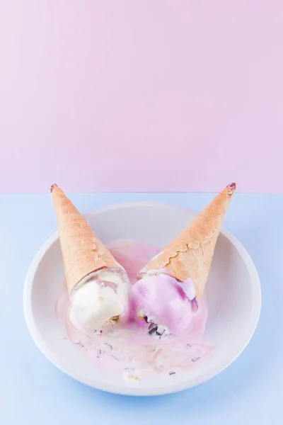Melted ice cream on a pink blue background. Two ice cream cones on a white plate. Summer milk dessert in a waffle cone. Summer concept
