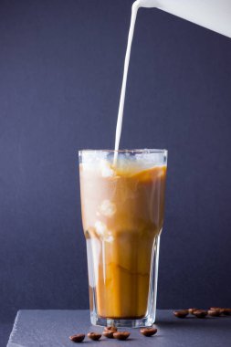 Koyu bir arka plan üzerinde süt ile buzlu kahve. Tahtada kafeinli yaz içkisi. Latte cam bir fincan ve kahve çekirdekleri içinde. Kopyalama alanı