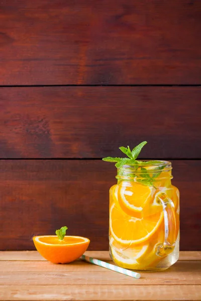 Fruit infused water with orange, lemon and mint. Mug delicious refreshing drink of mix fruits with mint on wooden boards. Iced summer drink in mason jar. Fresh homemade lemonade