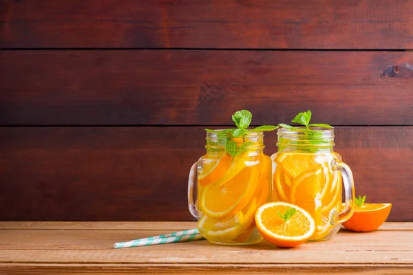 Fruit infused water with orange, lemon and mint. Mug delicious refreshing drink of mix fruits with mint on wooden boards. Iced summer drink in mason jar. Fresh homemade lemonade