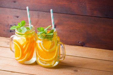 Meyve portakal, limon ve nane ile su aşılanmış. Ahşap tahtalar üzerinde mason kavanozda buzlu yaz içkisi. Taze ev yapımı limonata