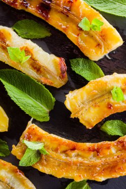 Siyah mutfak tahtası ve şist taşı üzerinde ızgara muz yarım. Siyah arka planda nane ile Fırında muz tatlısı. Asya sağlıklı gıda. Görünümü kapat